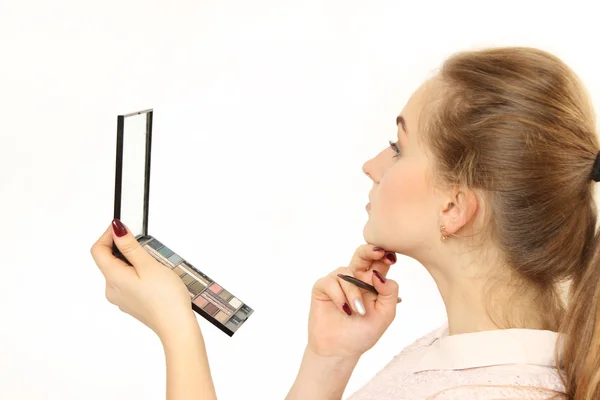 Joven chica hace un maquillaje delante de un pequeño espejo cosmético . — Foto de Stock