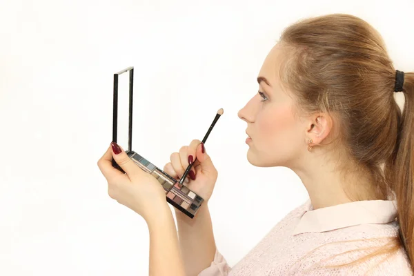 Joven chica hace un maquillaje delante de un pequeño espejo cosmético . — Foto de Stock