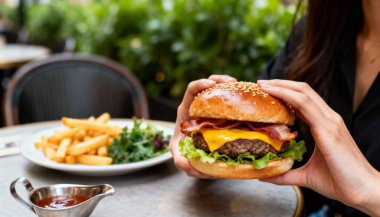 Kadın eli, susamlı ve domatesli beyaz ahşap bir arka planda lezzetli bir hamburger tutuyor..