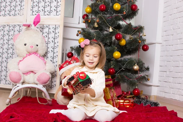 the girl with a toy engine and gifts under a Christmas fir-tree