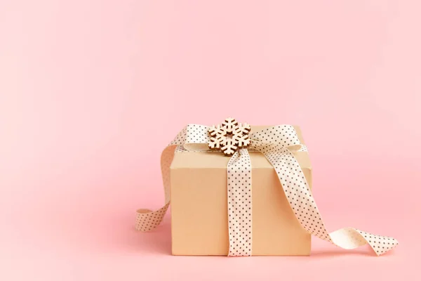 Kraft geschenkdoos met lint strik en sneeuwvlokken op pastelroze achtergrond met plaats voor tekst. kopieer ruimte kerstkaart — Stockfoto