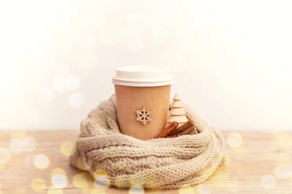 Xícara de papel com café em um cachecol acolhedor de malha com flocos de neve em um fundo de madeira — Fotografia de Stock