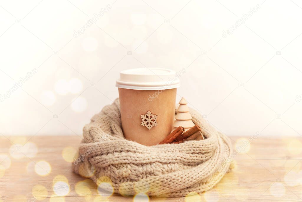 paper cup with coffee in a knitted cozy scarf with snowflakes on a wooden background