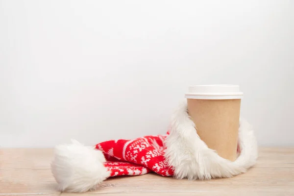 Xícara de papel de café embrulhado em um chapéu de Papai Noel em um fundo de Natal branco e de madeira. — Fotografia de Stock