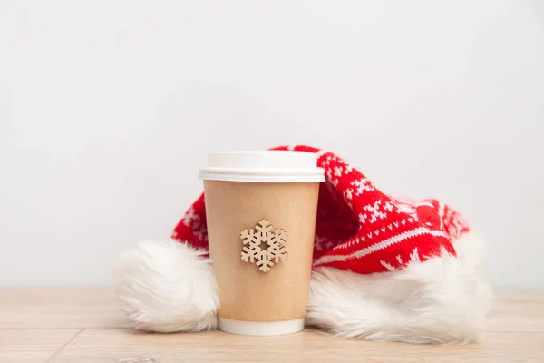 Бумажная чашка кофе, завернутая в шляпу Санты на белом и деревянном рождественском фоне. — стоковое фото