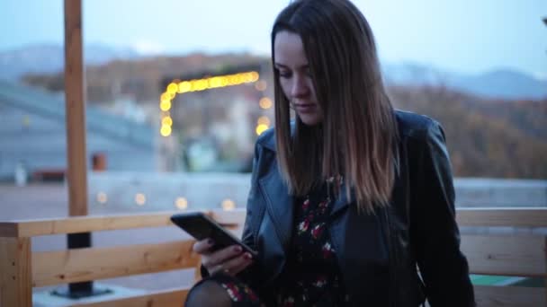Νεαρή κοπέλα χρησιμοποιεί ένα smartphone το βράδυ σε ένα καφέ. γυναίκα που μιλάει — Αρχείο Βίντεο