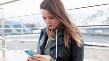 ... modaya uygun günlük giysiler içinde genç, şık, uzun saçlı bir kadın sokakta oturuyor ve telefonunu kullanıyor. Güzel ve çekici bir kız cep telefonuyla konuşuyor..