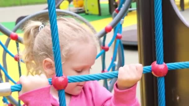 Liten aktiv söt kaukasisk blond lockig flicka på lekplatsen klättrar på sport komplex. unge på ett gungbo i en förskola — Stockvideo