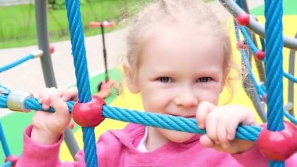 Liten aktiv söt kaukasisk blond lockig flicka på lekplatsen klättrar på sport komplex. unge på ett gungbo i en förskola — Stockvideo