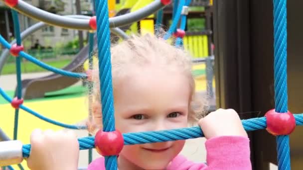 Liten aktiv söt kaukasisk blond lockig flicka på lekplatsen klättrar på sport komplex. unge på ett gungbo i en förskola — Stockvideo