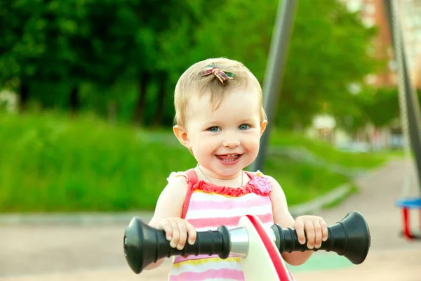 Little funny baby girl smiling and swinging on swing on playground. happy kid outdoors at park summer. Copyspace — Stock Photo, Image