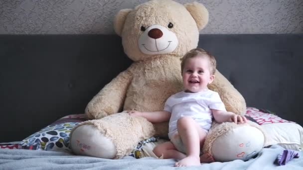 Mignon petit enfant souriant jouant avec son gros ours en peluche sur le lit. Petit garçon et jouet — Video