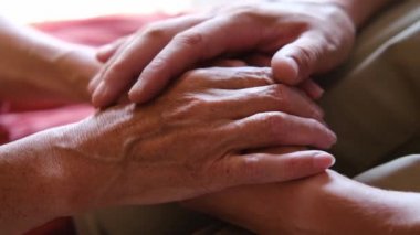 Endişeli beyaz bir adam, yaşlı hasta annesinin şefkatini ya da sevgisini nazikçe okşuyor. Oğul, yaşlı annenin kırışık koluyla yatakta oturuyor. Adam eski ebeveynine destek oluyor..