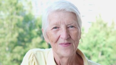 Closeup smiling caucasian senior woman posing at camera in summer day in garden. Senior lady looking straight. Older woman Female model standing outdoors alone slow motion