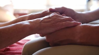 Endişeli beyaz bir adam, yaşlı hasta annesinin şefkatini ya da sevgisini nazikçe okşuyor. Oğul, yaşlı annenin kırışık koluyla yatakta oturuyor. Adam eski ebeveynine destek oluyor..