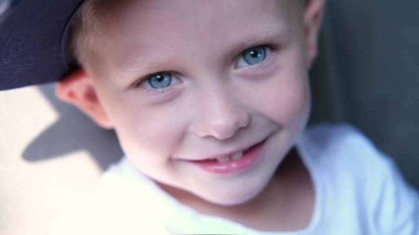 Портрет белого милого голубоглазого мальчика, улыбающегося и смеющегося, сидя в машине в солнечный день. Счастливые дети путешествуют на машине — стоковое видео