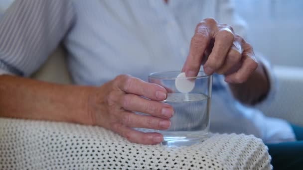 Close up painkiller tablet dissolves in glass on table in hand elderly woman. old woman has a cold. healthcare medication process concept. — Stock Video