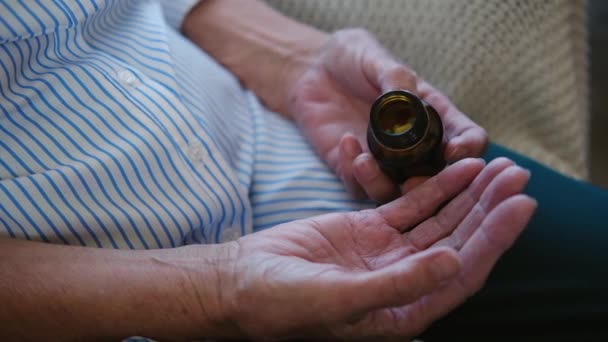 Крупним планом рука старшої дорослої жінки тримає таблетки для знеболювання, що заливає дві капсули з пляшки медикаментів. літня бабуся приймає ліки. охорона здоров'я. концепція фармації та лікування — стокове відео