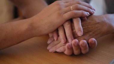 Endişeli beyaz bir adam, yaşlı hasta annesinin şefkatini ya da sevgisini nazikçe okşuyor. Oğul, yaşlı annenin kırışık koluyla yatakta oturuyor. Adam eski ebeveynine destek oluyor..