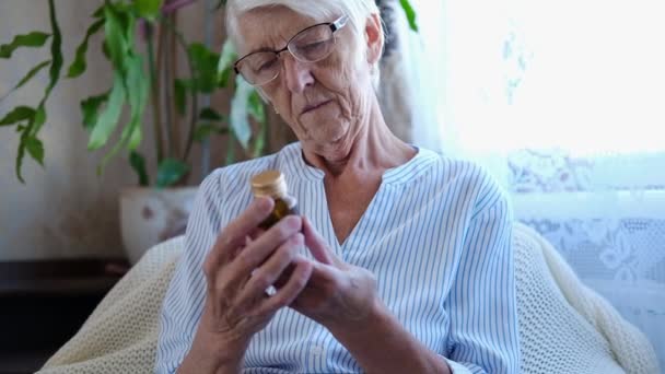 Stara, kaukaska starsza kobieta czyta etykietę z lekami i nalewa dwie tabletki z butelki. opieka zdrowotna dla osób starszych, koncepcja apteki, zbliżenie. Portret babci — Wideo stockowe
