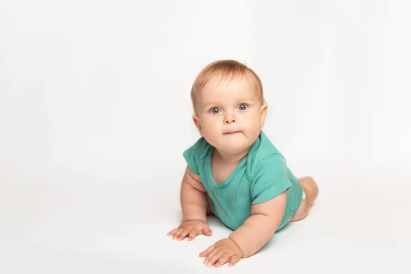 Mignon petit caucasien tout-petit bébé garçon ramper sur le plancher du studio blanc. Un petit enfant souriant portant un t-shirt vert explore le monde. Concept de garde et d "éducation des enfants. — Photo