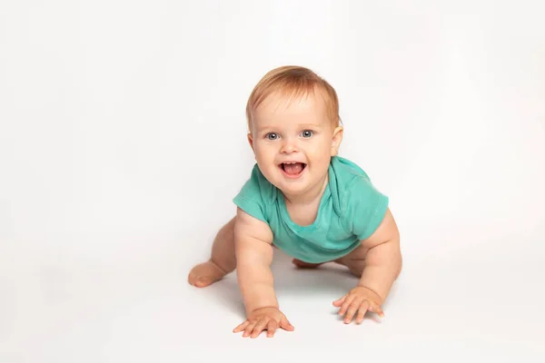 Mignon petit caucasien tout-petit bébé garçon ramper sur le plancher du studio blanc. Un petit enfant souriant portant un t-shirt vert explore le monde. Concept de garde et d "éducation des enfants. — Photo