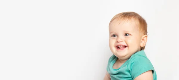 Малыш в зеленой футболке смеется, глядя на камеру на белом фоне. Концепция ухода за детьми и воспитания. — стоковое фото