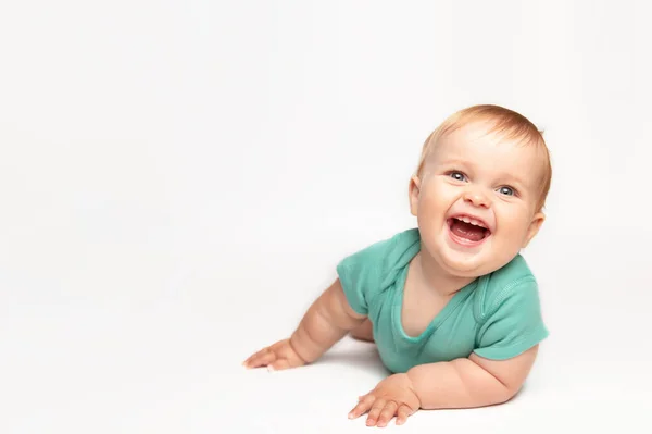 Carino piccolo bambino caucasico bambino strisciare sul pavimento bianco dello studio. Un bambino sorridente che indossa una maglietta verde esplora il mondo. Concetto di infanzia e educazione. — Foto Stock