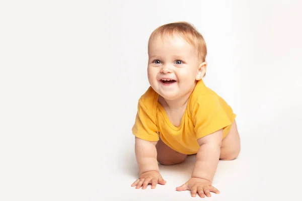 작은 악어의 작은 아기 아기가 흰색 스튜디오 바닥에서 기어 다닌다. 노란 티셔츠를 입은 어린 아기가 세상을 탐험하는 모습. 육아와 양육 개념. — 스톡 사진