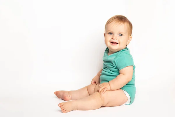 Enfant bébé bébé garçon portant un t-shirt vert rit heureux en regardant la caméra isolée assise sur un fond blanc. Concept de garde et d "éducation des enfants. — Photo