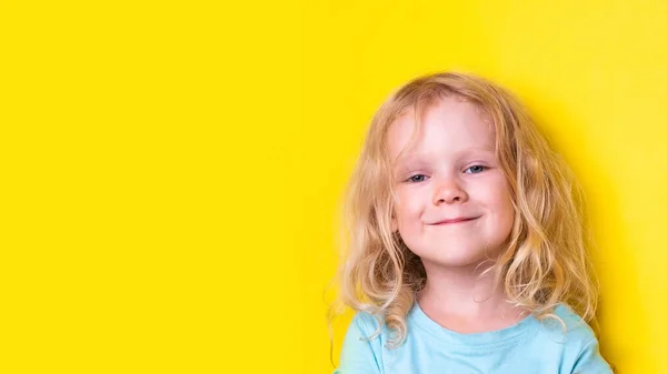 노란색 배경에 복제 공간 이 있는 파란 티셔츠를 입은 금발 머리의 아름다운 곱슬곱슬 한 작은 소녀 사진 — 스톡 사진