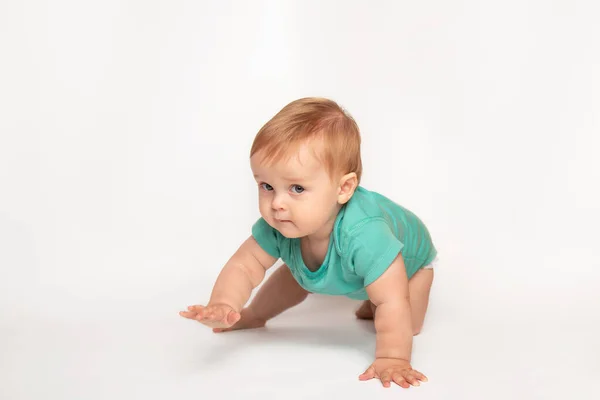 Mignon petit caucasien tout-petit bébé garçon ramper sur le plancher du studio blanc. Un petit enfant souriant portant un t-shirt vert explore le monde. Concept de garde et d "éducation des enfants. — Photo