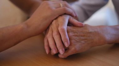 Endişeli beyaz bir adam, yaşlı hasta annesinin şefkatini ya da sevgisini nazikçe okşuyor. Oğul, yaşlı annenin kırışık koluyla yatakta oturuyor. Adam eski ebeveynine destek oluyor..