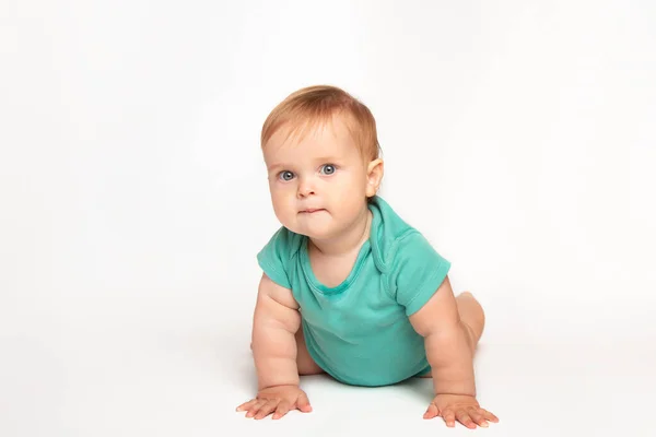 Mignon petit caucasien tout-petit bébé garçon ramper sur le plancher du studio blanc. Un petit enfant souriant portant un t-shirt vert explore le monde. Concept de garde et d "éducation des enfants. — Photo