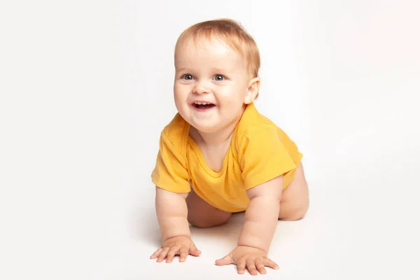 Mignon petit caucasien tout-petit bébé garçon ramper sur le plancher du studio blanc. Un petit enfant souriant portant un t-shirt jaune explore le monde. Concept de garde et d "éducation des enfants. — Photo