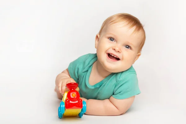 Bayi laki-laki cantik yang lucu menggulung mobil mainan di lantai. Anak bermain dengan mainan kereta api. masa kecil, anak-anak dan konsep orang Stok Foto