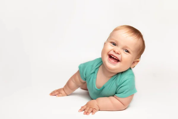 Mignon petit caucasien tout-petit bébé garçon ramper sur le plancher du studio blanc. Un petit enfant souriant portant un t-shirt vert explore le monde. Concept de garde et d "éducation des enfants. — Photo