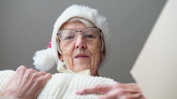 Primer plano dentro de la caja de cartón vista inferior, mujer anciana que usa el paquete de embalaje del sombrero de Navidad con el regalo de punto a cuadros para nietos o hijos se siente feliz. concepto de entrega urgente — Vídeos de Stock