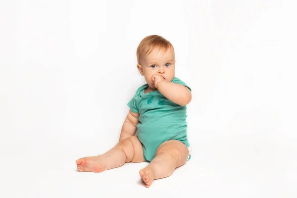 Mignon caucasien un an bébé suce pouce et gratte ses premières dents. tout-petit garçon taquinant sur fond blanc en studio. concept de garde d'enfants et de santé infantile — Photo