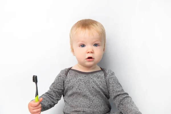 Retrato pequeño caucásico lindo bebé rubio sorprendido con un cepillo de dientes mirando a la cámara. niño sobre fondo blanco cepillándose los dientes con un cepillo de color — Foto de Stock