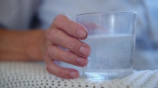 Close-up pijnstiller tablet lost op in glas op tafel bij hand oudere vrouw. Oude vrouw is verkouden. geneesmiddelenprocesconcept voor gezondheidszorg. — Stockvideo