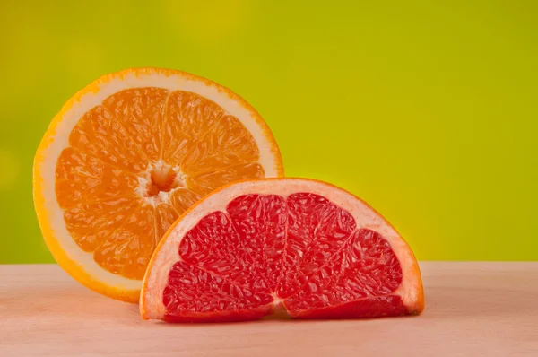 Оранжевый и грейпфрутовый ломтики на деревянной доске с желтым фоном — стоковое фото