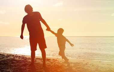silhouettes of father and son having fun at sunset clipart