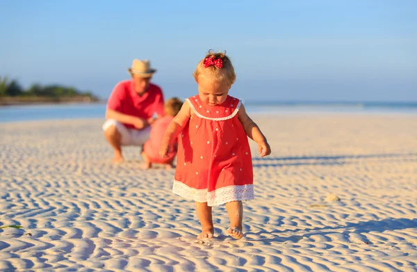 Petite fille faire les premiers pas à la plage avec la famille sur fond — Photo