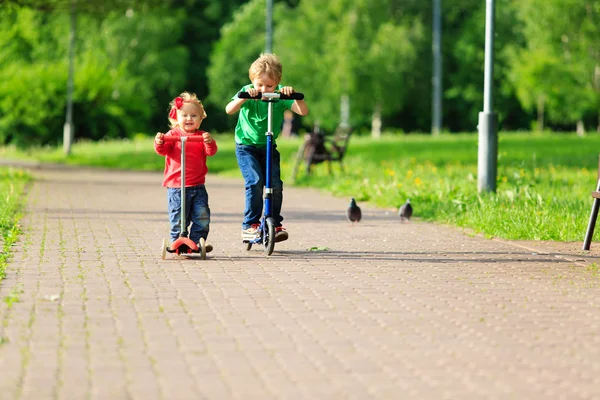 Kis fiú- és kisgyermek lány lovaglás szkuterek (robogók), nyáron — Stock Fotó