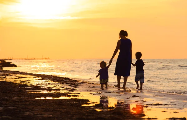 Mãe e dois filhos andando na praia ao pôr do sol — Fotografia de Stock