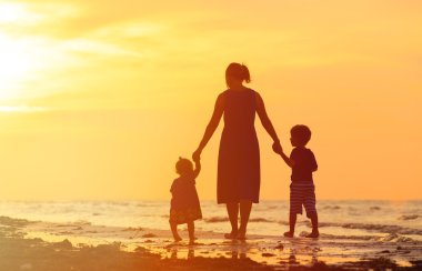 Anne ve iki çocuğu batımında sahilde yürüyüş
