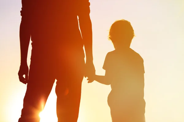 Sylwetka ojca i syna trzymających się za ręce o zachodzie słońca — Zdjęcie stockowe