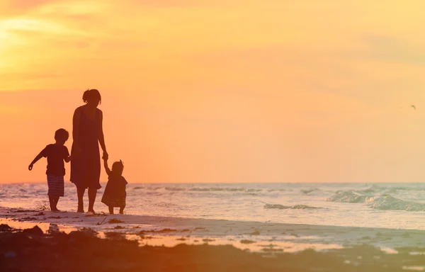 Mère et deux enfants marchant à la plage du coucher du soleil — Photo