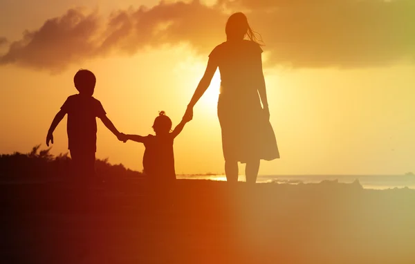 Mor och två barn gå på stranden vid solnedgången — Stockfoto